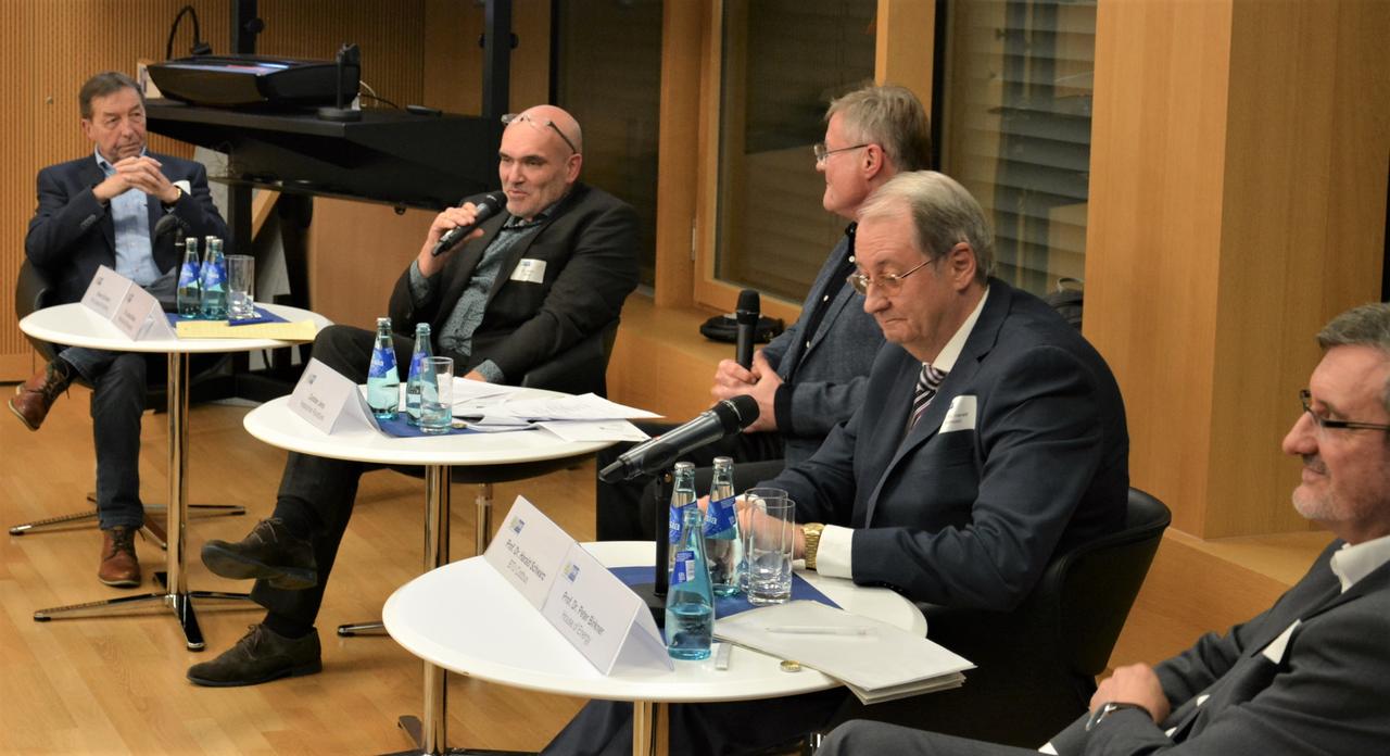 Fünf Männer auf Stühlen mit Mikrofonen