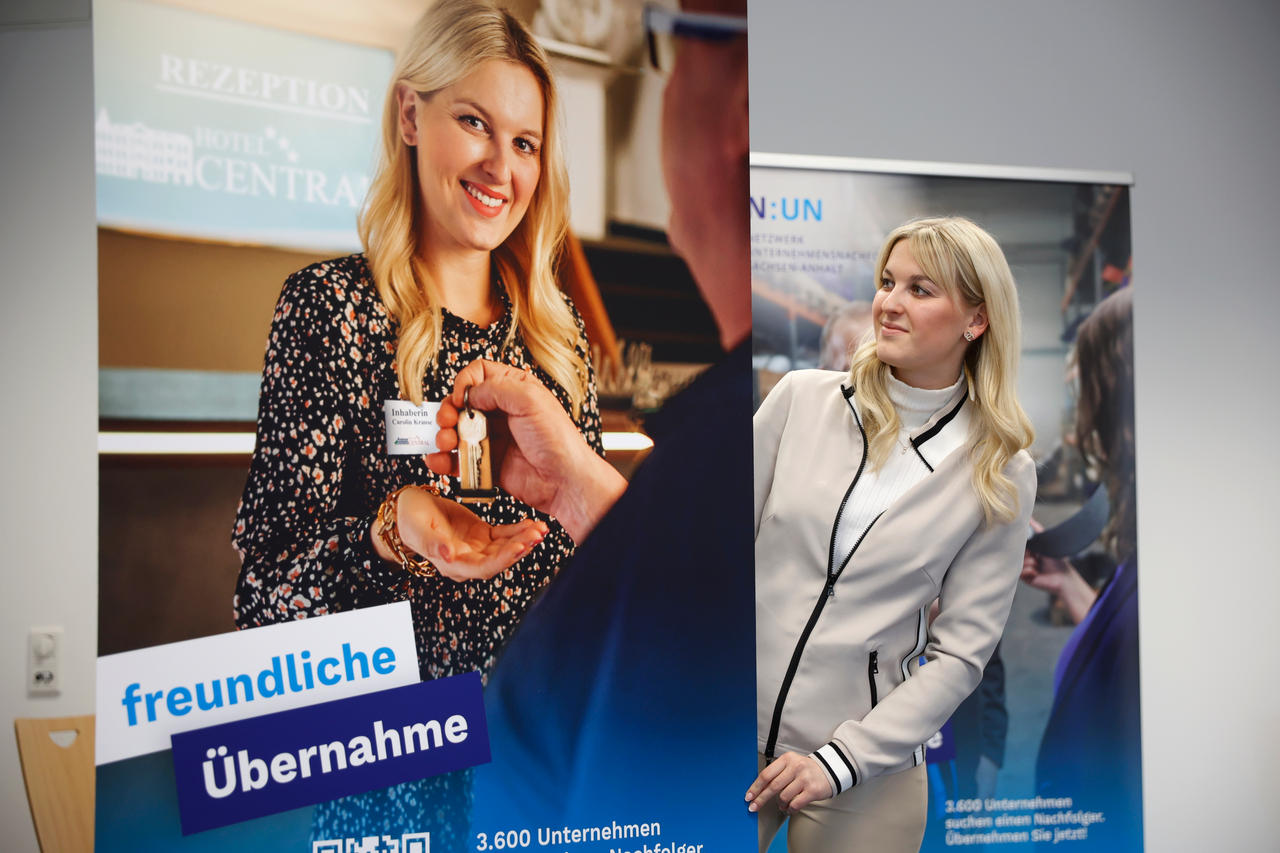 Frau schaut seitlich auf ein Roll-Up, hier ist sie auch abgebildet und bekommt einen Schlüssel überreicht