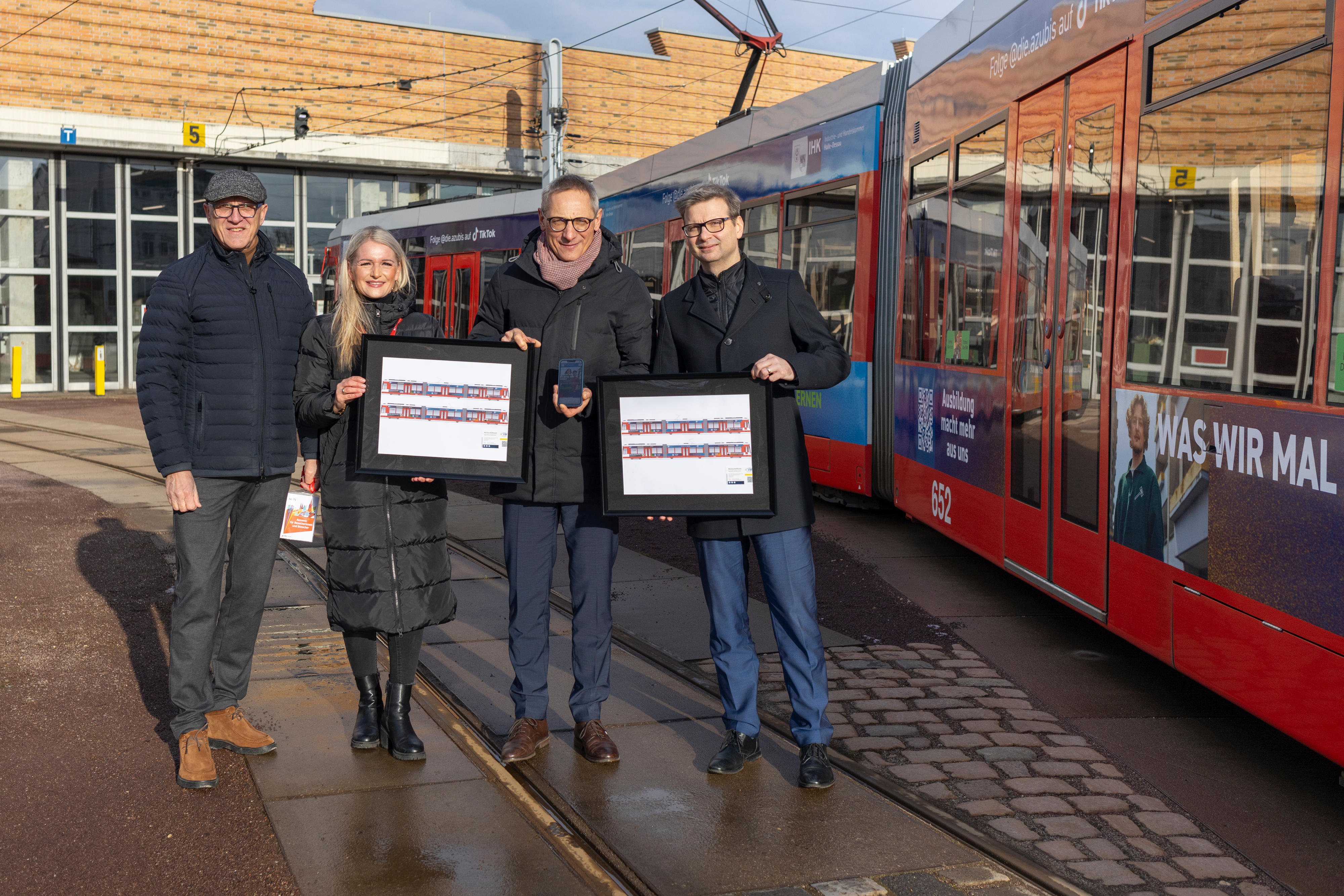 drei Herren und eine Dame stehen vor einer Straßenbahn und schauen in die Kamera