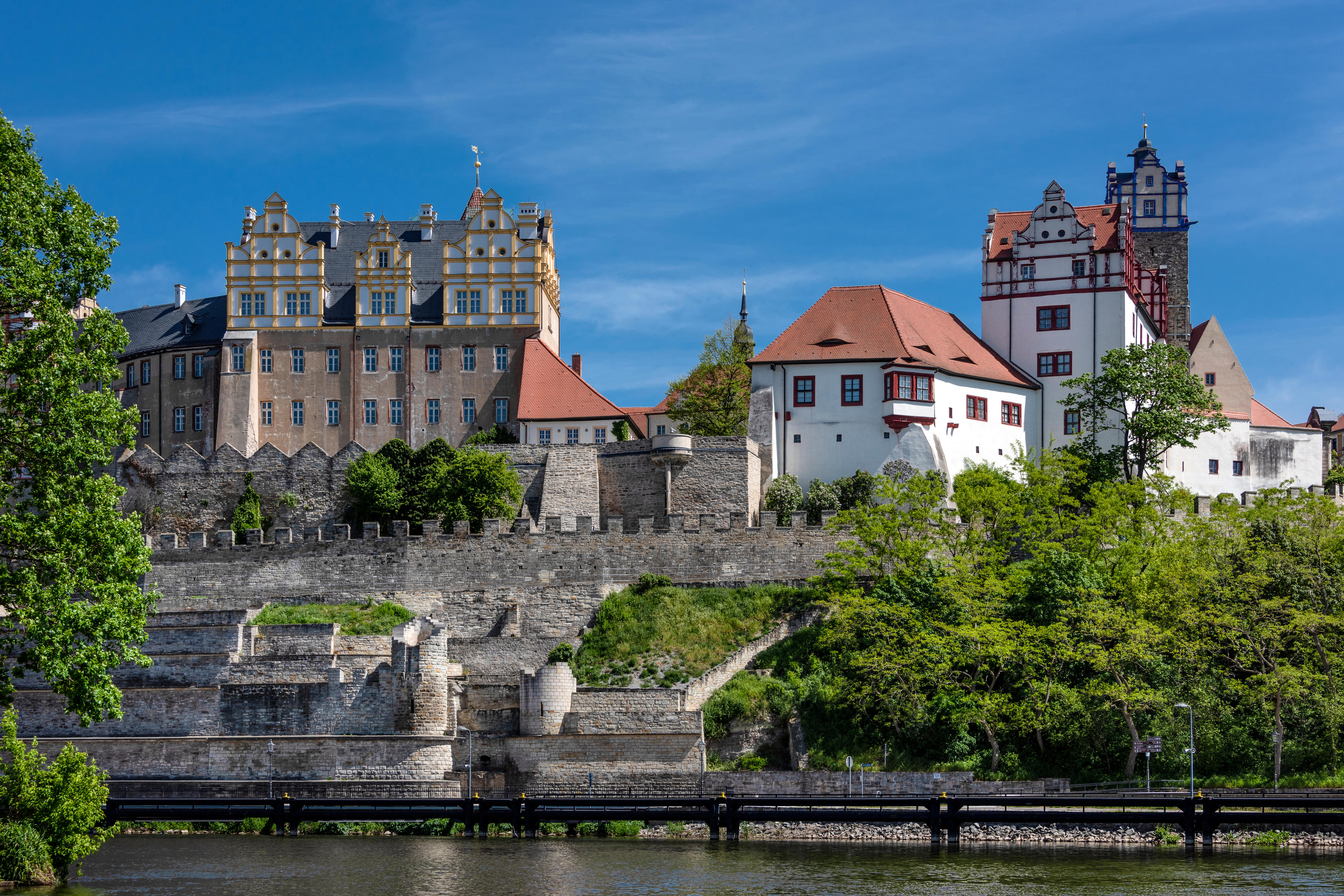 Schlossanlage mit Stadtmauer auf H&uuml;gel &uuml;ber Fluss, blauer Himmel