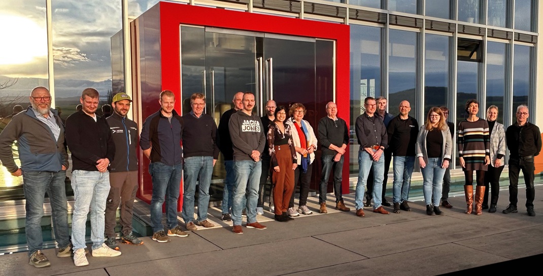 Eine Gruppe von Menschen steht vor einem roten Geb&auml;ude.