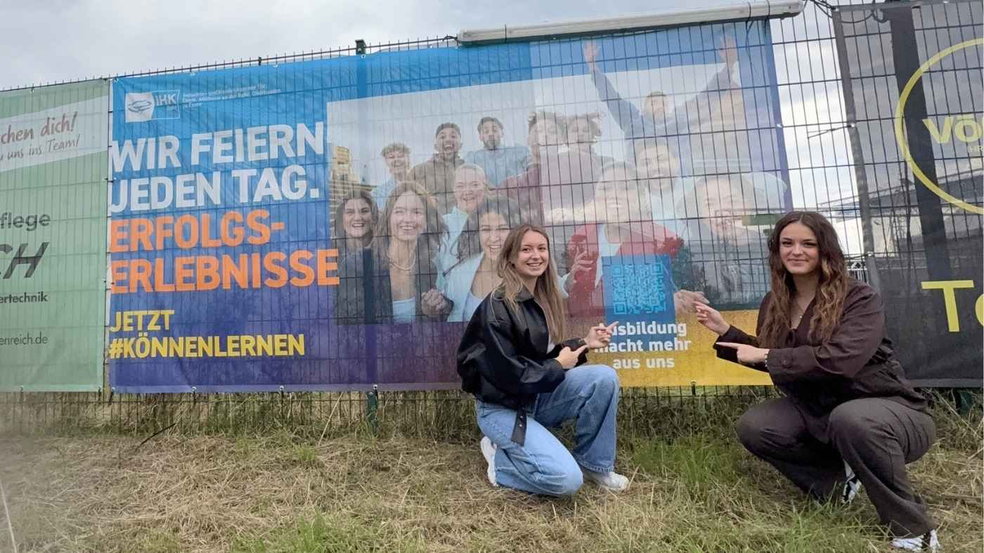 Zwei Auszubildende der IHK Essen vor einem Bauzaun-Banner der #könnenlernen Ausbildungs-Kampagne