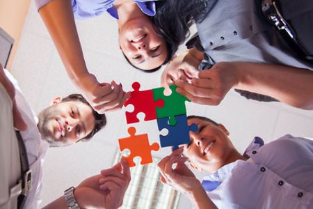 Frauen und M&auml;nner halten 4 Puzzleteile aneinander. 