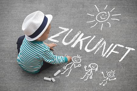 Kind schreibt mit Stra&szlig;enkreide das Wort Zukunft