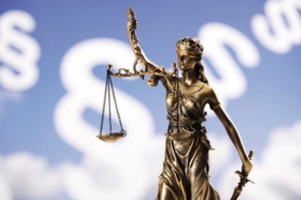 Justitia-Statuette vor Hintergrund mit Paragraphen