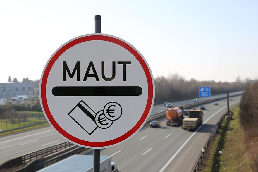 Schild mit Aufschrift 'Maut', im Hintergrund 6spurige befahrene Autobahn