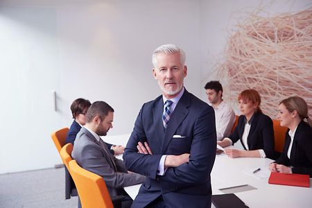 Ein Mann steht vor einem Tisch an dem mehrere Personen sitzen.
