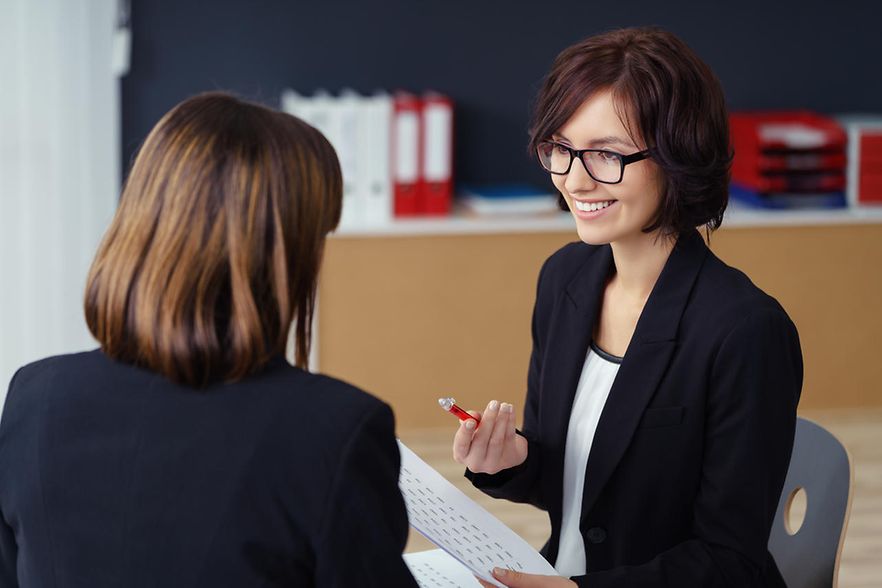 Zwei Gesch&auml;ftsfrauen sitzen an einem Tisch und kommunizieren miteinander.