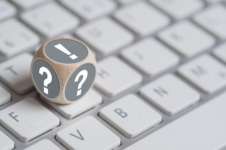 Ein grauer W&uuml;rfel mit Fragezeichen und Ausrufezeichen auf einer wei&szlig;en Tastatur.