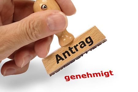Eine Hand h&auml;lt einen Stempel mit Antrag genehmigt.