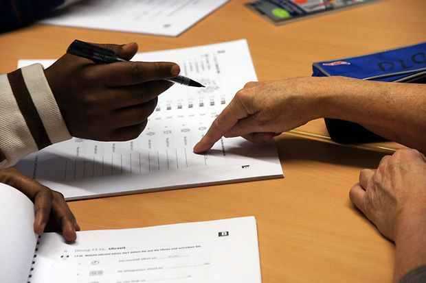 Lehrerin zeigt auf Unterlagen, während sie einem Schüler eine Aufgabe im Deutschkurs für Flüchtlinge erklärt