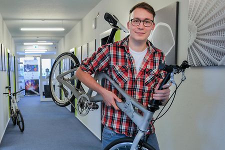 Ein junger Mann h&auml;lt ein Fahrrad in den H&auml;nden.