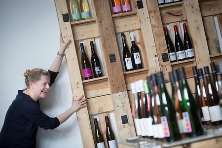 Eine lachende Frau lehnt sich an ein Weinregal.