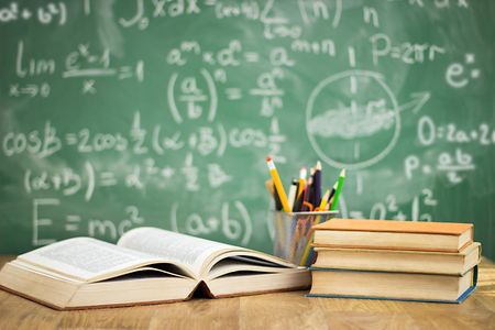 Vor einer Schultafel liegen B&uuml;cher und dahinter ein Beh&auml;lter mit Stiften