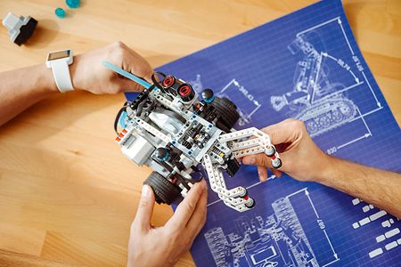 Drei H&auml;nde halten ein Modell aus Lego-Spielzeug