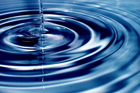 Das Bild einen Wasserstrahl und dadurch entstandene Ringe im Wasser.