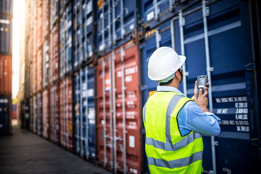 Ein Mann erfasst mit einem technischen Ger&auml;t einen Container in einem Containerhafen.