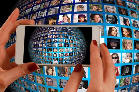 Frau h&auml;lt Smartphone - im Hintergrund viele Gesichter