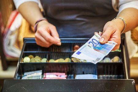Frau, die Bargeld in eine Kasse legt