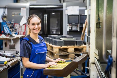 L&auml;chelnde Frau im Blaumann vor einer CNC-Maschine
