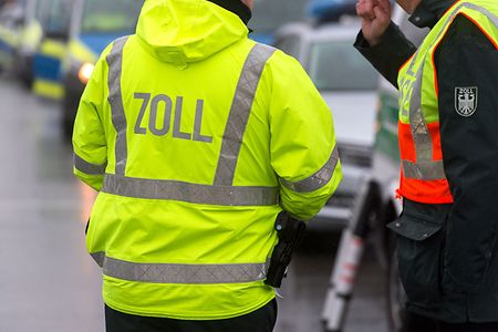 M&auml;nner in Warnwesten mit der Aufschrift Zoll stehen auf der Stra&szlig;e