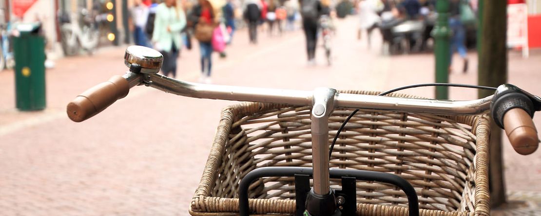 Ein Fahrrad mit einem Einkaufskorb am Lenker steht in einer Fu&szlig;g&auml;ngerzone mit Passanten