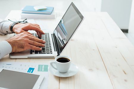 Unternehmer am Laptop mit Kafetasse.