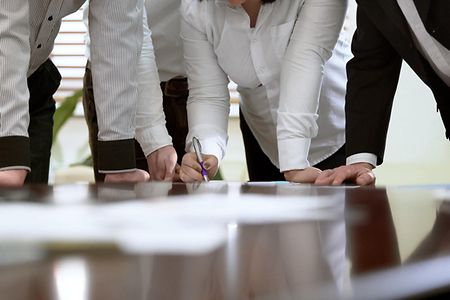Personen in einer Besprechung st&uuml;tzen ihre Arme auf einen Besprechungstisch