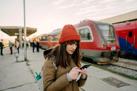Junge Frau mit Smartphone am Bahnhof