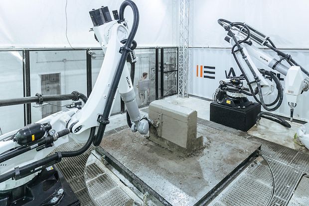 Roboter drucken Betonteile mit einem Spritzverfahren auf einer Stahlpalette.