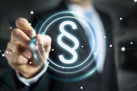 Paragraphensymbol; im Hintergrund Mann in Anzug mit Stift in der Hand