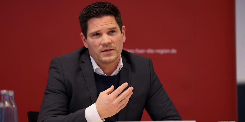 Thomas Alswede-Brech sitzt gestikulierend an einem Tisch und beantwortet Fragen. 