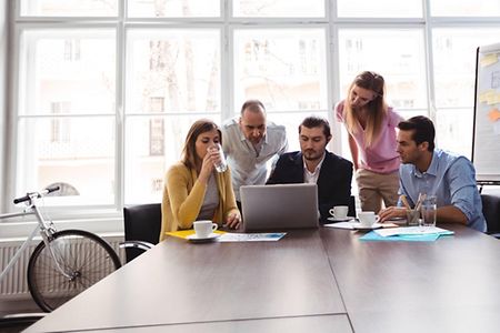 4 Personen sitzen vor Laptop und besprechen etwas