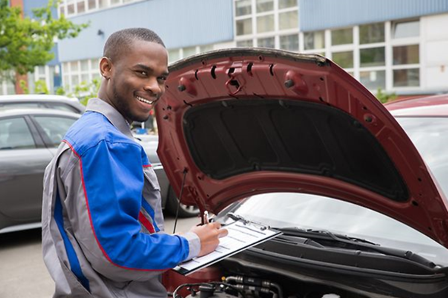 Junger Mitarbeiter checkt den Motor eines Autos