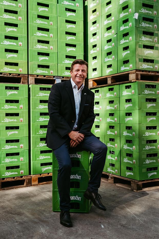 Norbert Lucks sitzend auf Bierkisten. Hinter ihm aufgestapelte Kisten.