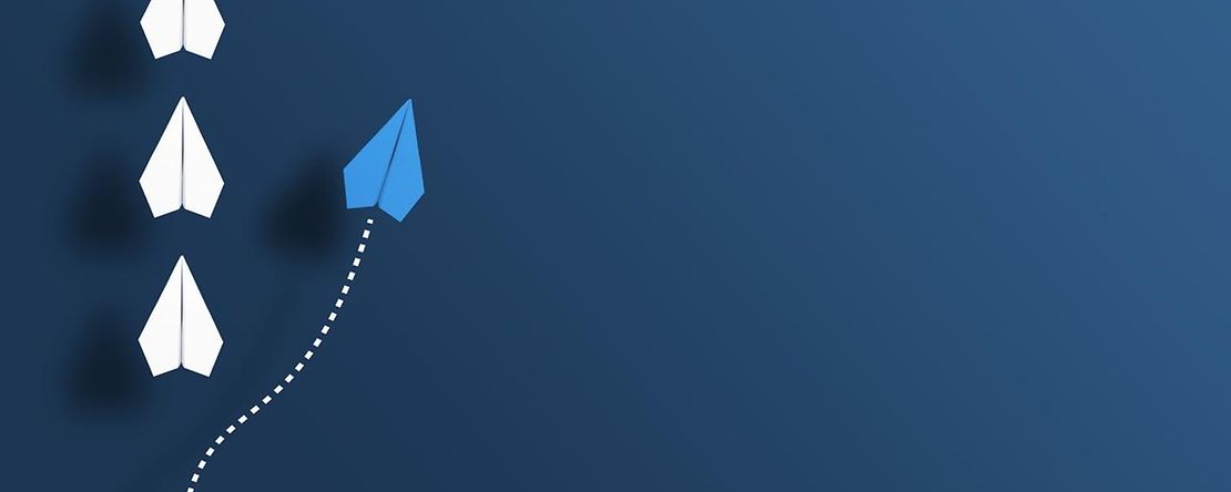 wei&szlig;e Papierflugzeuge in einer Reihe, ein blaues &uuml;berholt auf der rechten Seite.