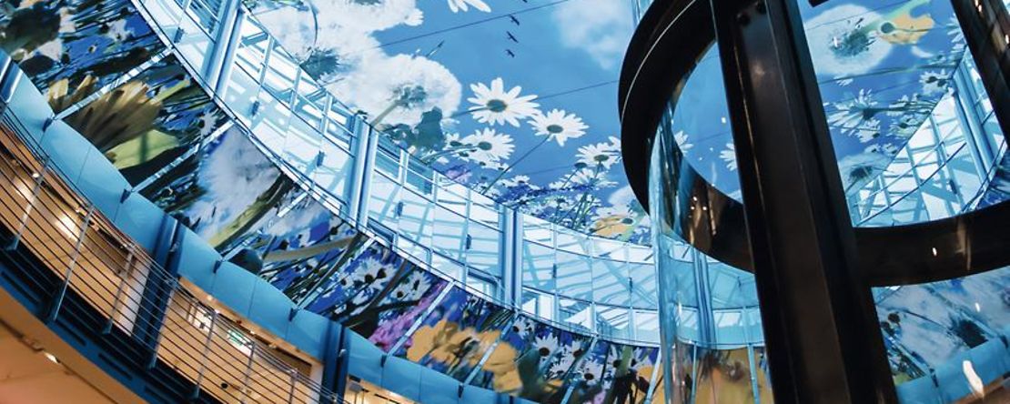 Gl&auml;serner Lift vor gl&auml;sernem Glasdach mit himmelblauem Blumen-Deko 