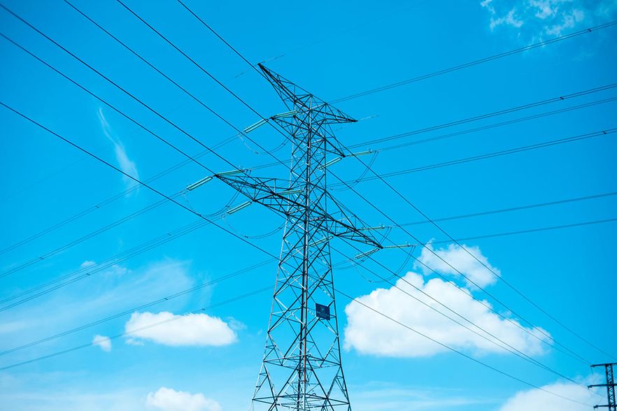 Strommast vor blauem Himmel mit wenigen Wolken.