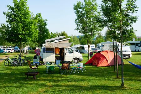 Campingplatz im Gr&uuml;nen mit Wohnmobil, Zelt und Campingst&uuml;hlen