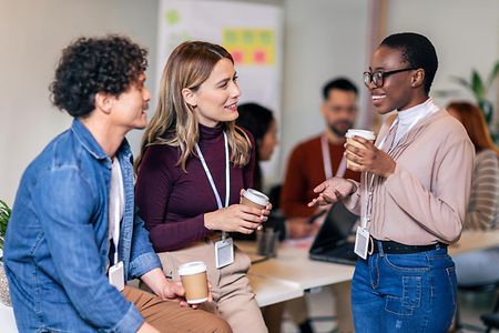 Drei Menschen unterhalten sich in einem B&uuml;ro und trinken dabei Kaffee