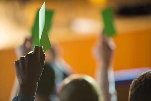 Nahaufnahme einer Hand, die während einer Abstimmung eine grüne Karte hochhält