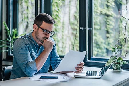 Worried businessman analyzing documents while working on laptop at table