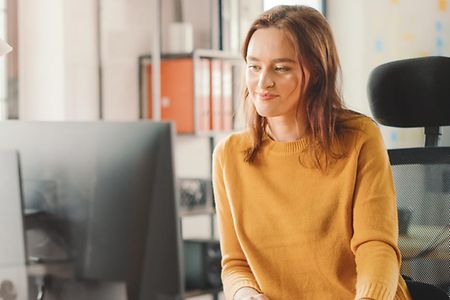 Eine junge Frau sitzt vor einem Computer am Arbeitsplatz