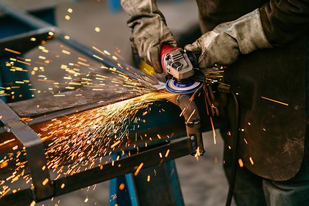 Factory worker grinding a metal structure with an angle grinder,sparks flying,close up.