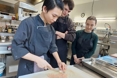 Sch&uuml;ler schauen dem K&uuml;chenprofi in einem Restaurant &uuml;ber die Schulter.