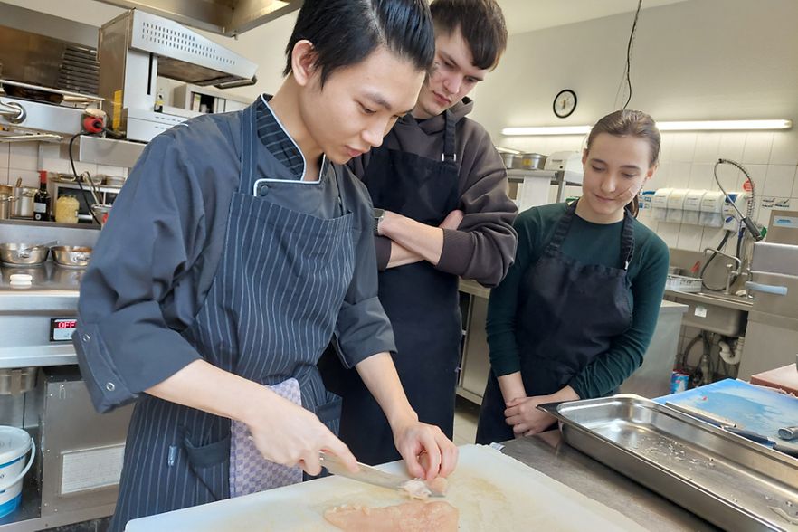 Sch&uuml;ler schauen dem K&uuml;chenprofi in einem Restaurant &uuml;ber die Schulter.