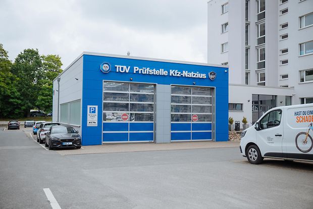 Ein blaues Gebäude, davor ein Parkplatz, auf dem einige Autos stehen.