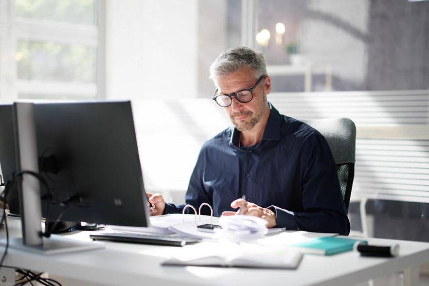 Dekoratives Bild: Person sitzt am Schreibtisch vor einem PC.