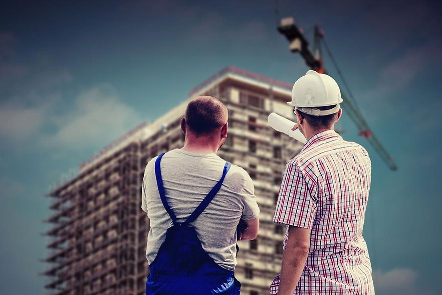 Zwei Personen schauen sich ein halb fertiges Geb&auml;ude auf einer Baustelle an. 