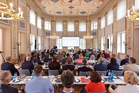 Menschen sitzen in einem Saal und h&ouml;ren einen Vortrag